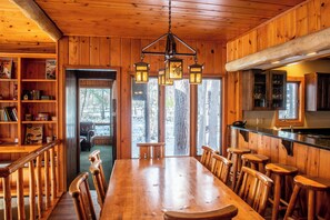 A wooden interior with a large dining table, bar stools, and a hanging light fixture.