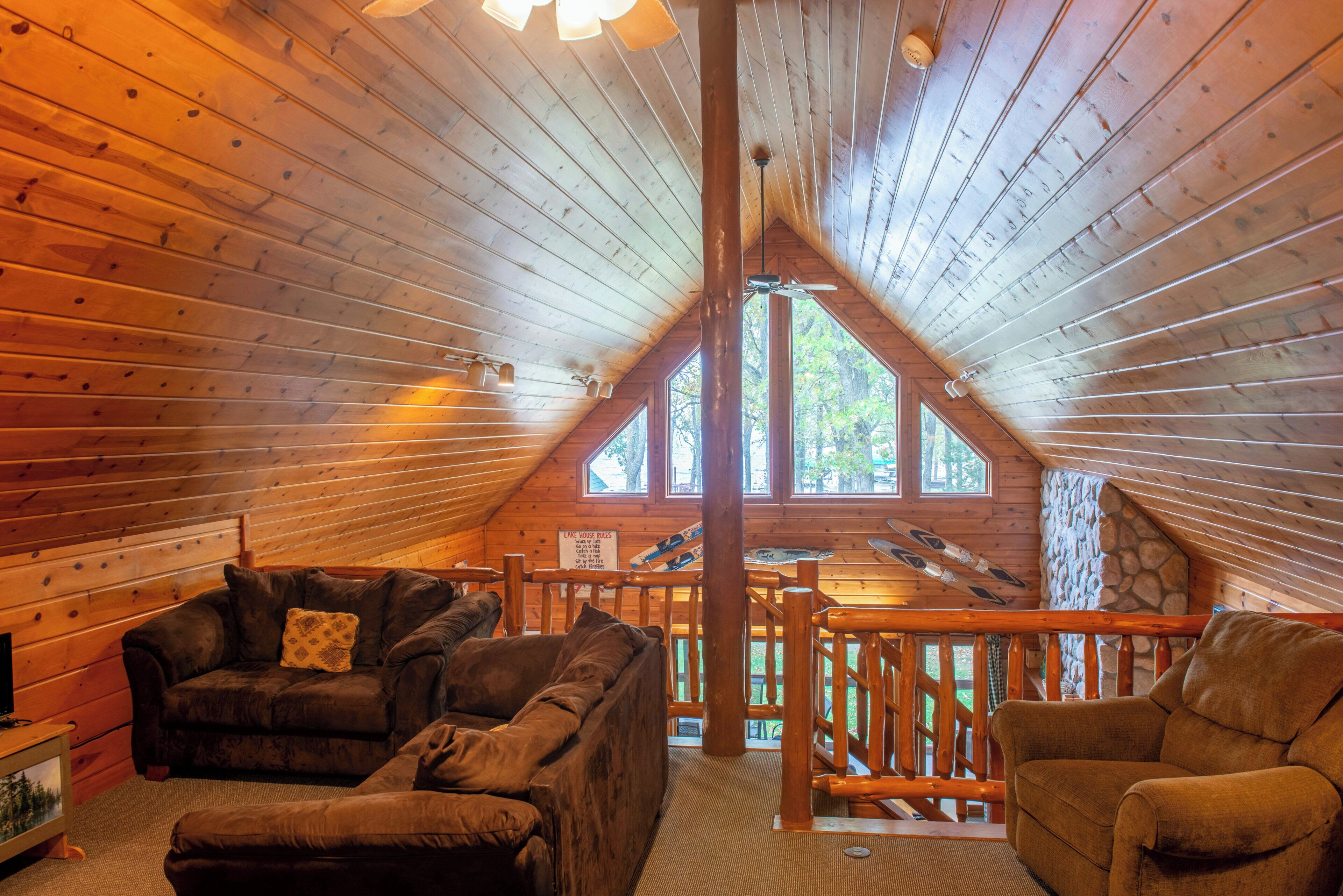 A log cabin interior with a loft area, wooden walls, and a stone wall.