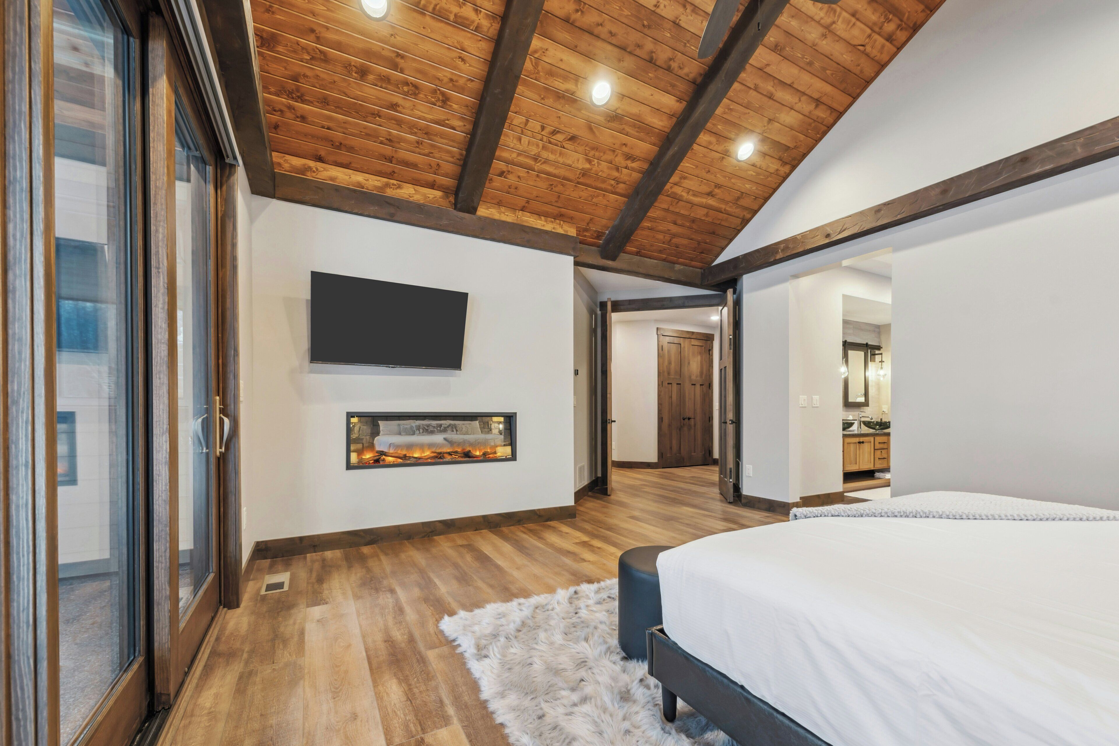 Quarto com teto de madeira, lareira, cama e televisão fixada na parede.