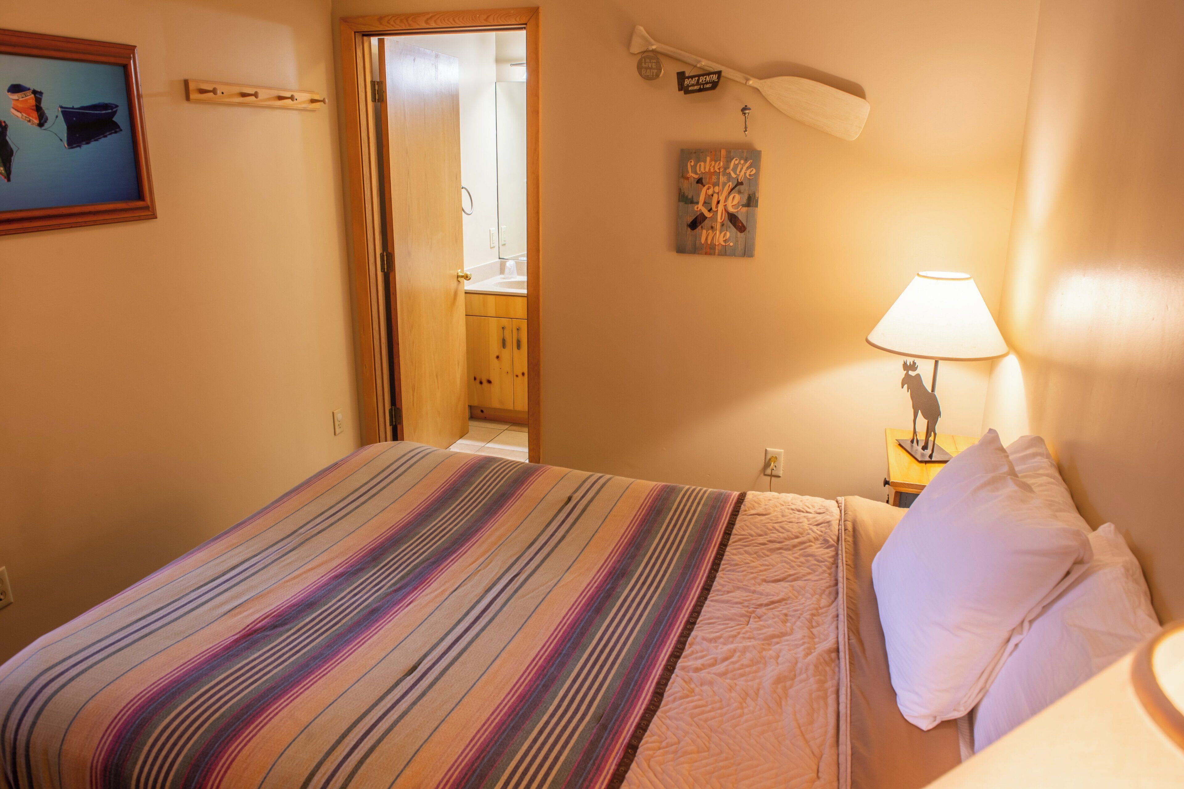 A hotel room with a bed, a nightstand with a lamp, a framed picture on the wall, and a door leading to a bathroom.