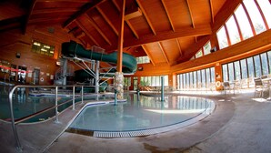 An indoor swimming pool with a slide, surrounded by large windows and a high ceiling.