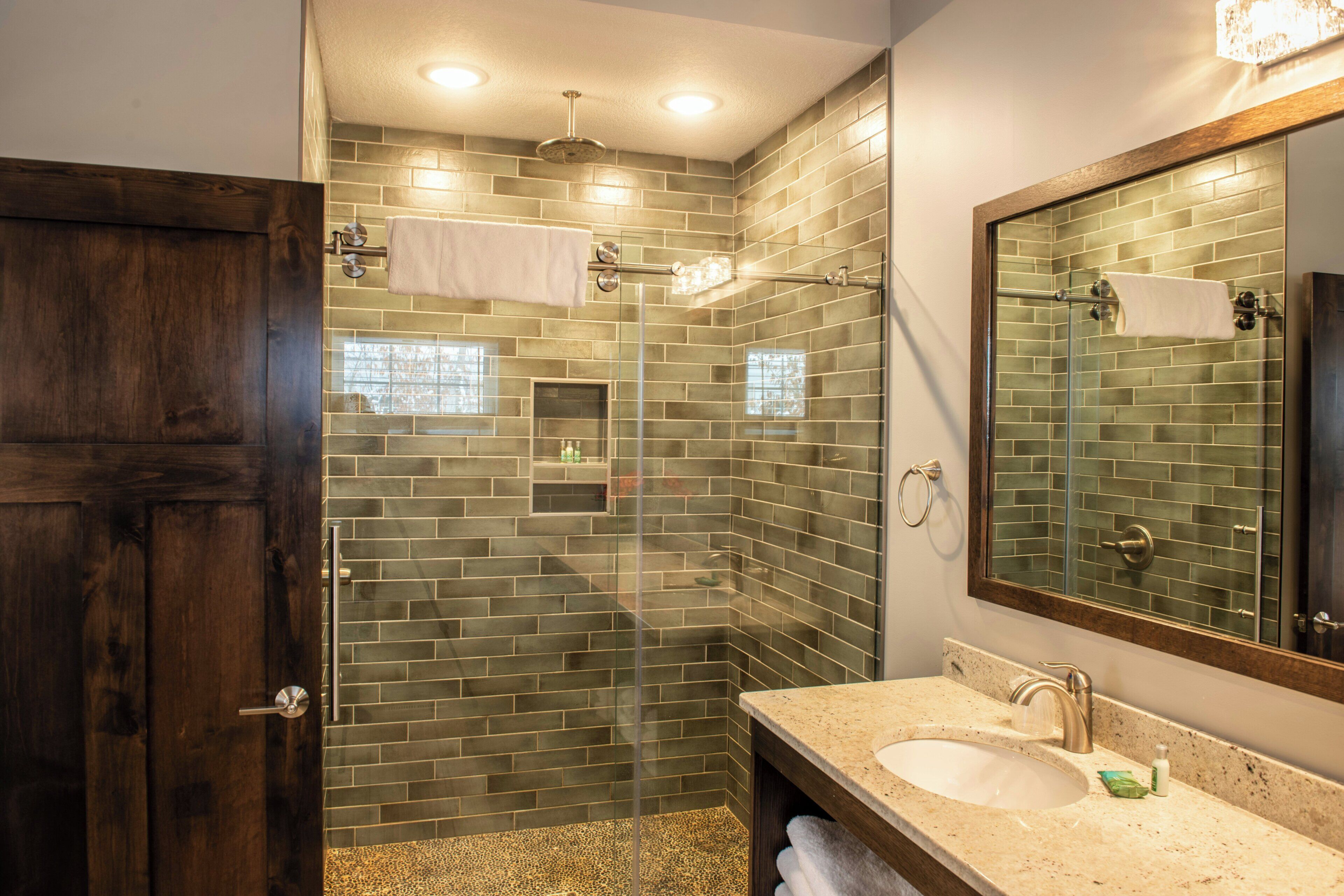 A bathroom with a glass-enclosed shower, a sink, and a mirror.