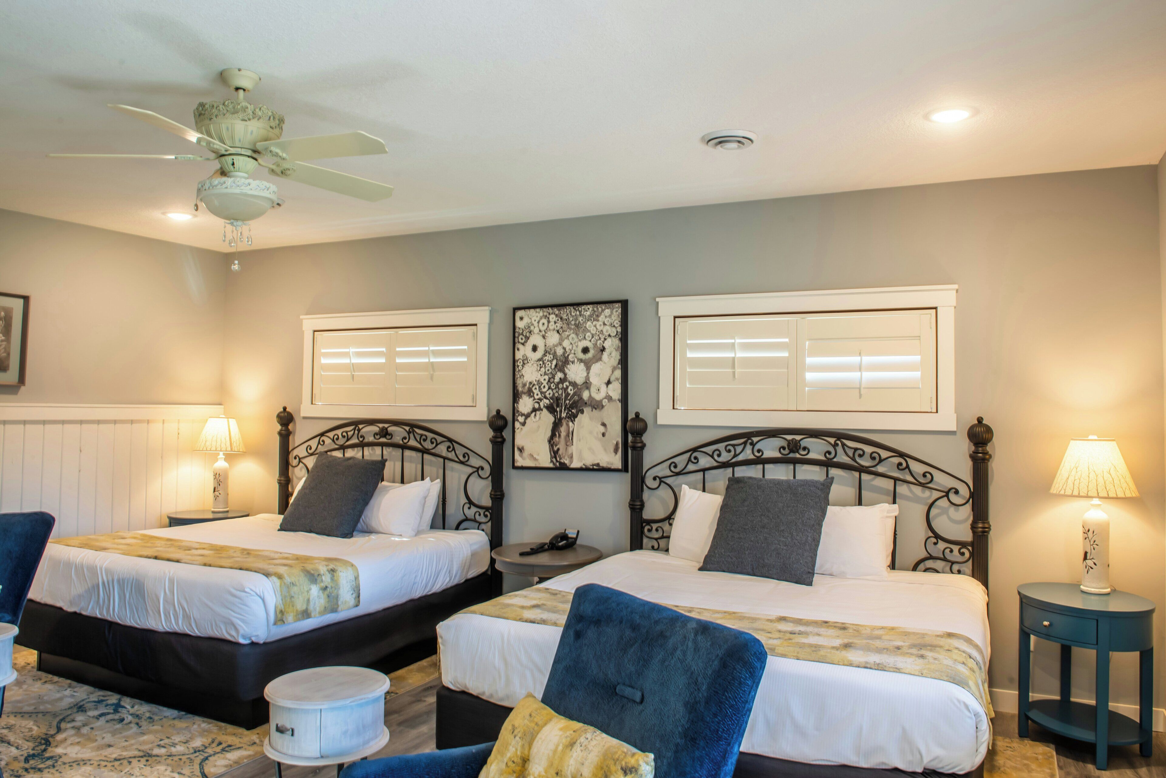 A hotel room with two beds, a ceiling fan, a round table, and a nightstand with a lamp.