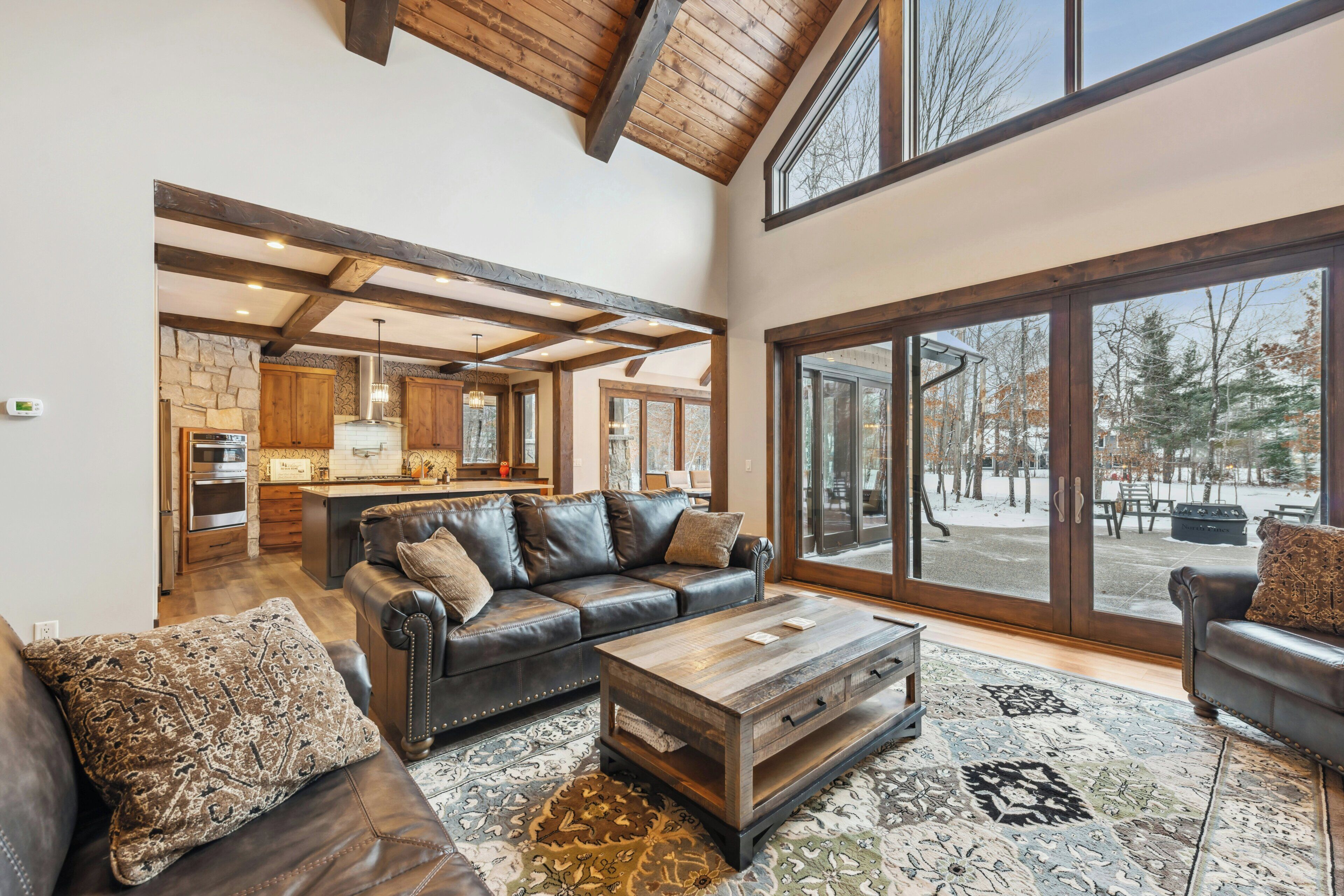 A spacious living room with a large window, a fireplace, and a kitchen area visible through an open door.