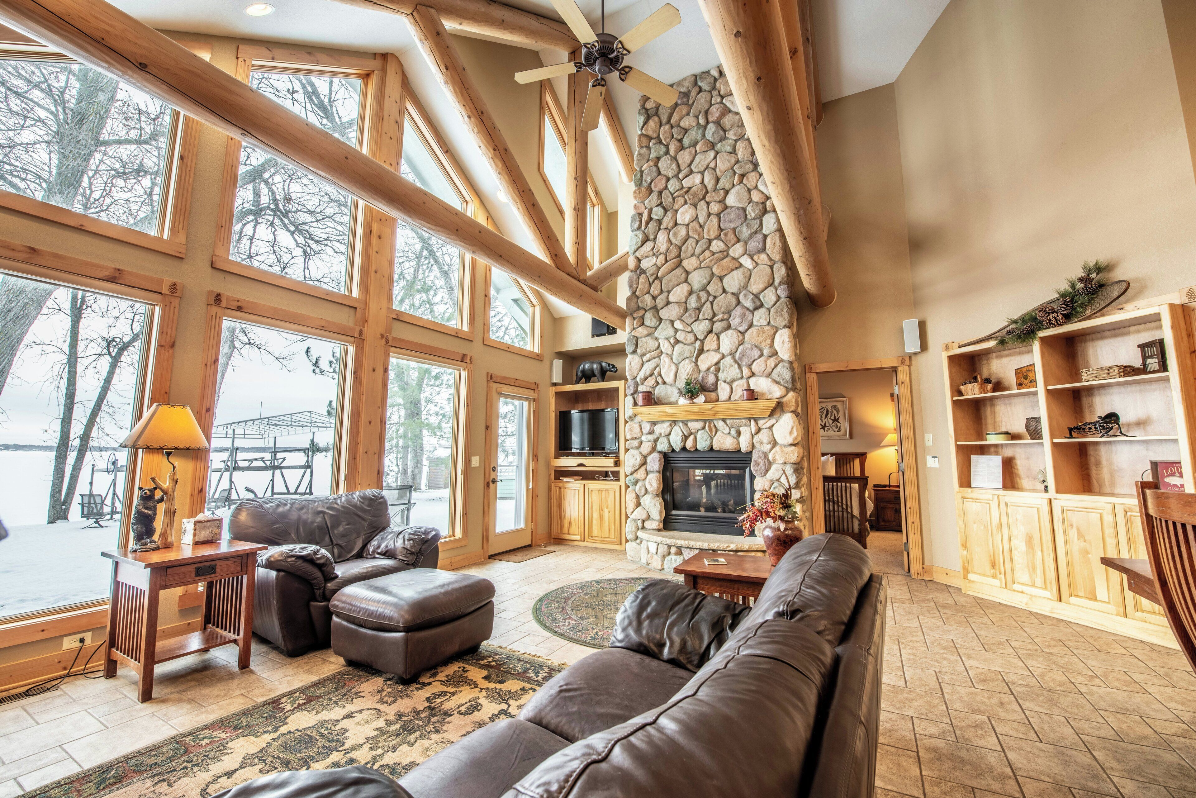 A spacious living area with a stone fireplace, large windows, and a cozy seating arrangement.