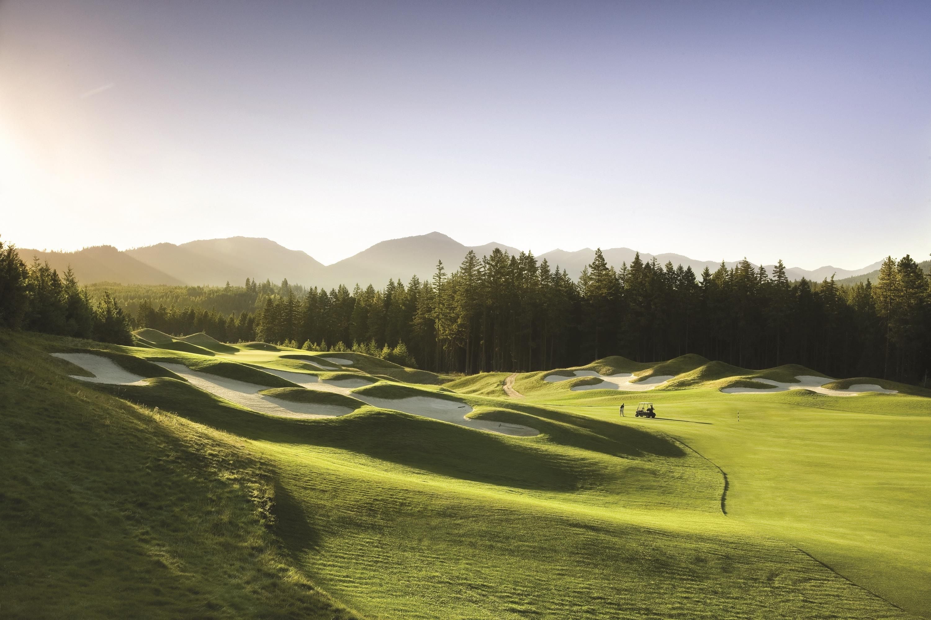 A golf course with sand bunkers, a clear sky, and distant mountains.