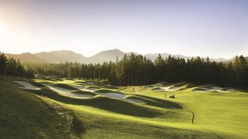 A golf course with sand bunkers, a clear sky, and distant mountains.