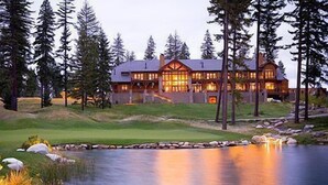 A large, multi-story lodge with a prominent central chimney, surrounded by a natural landscape including a pond and dense trees. - Suncadia Resort, a Destination by Hyatt Residence (Cle Elum)