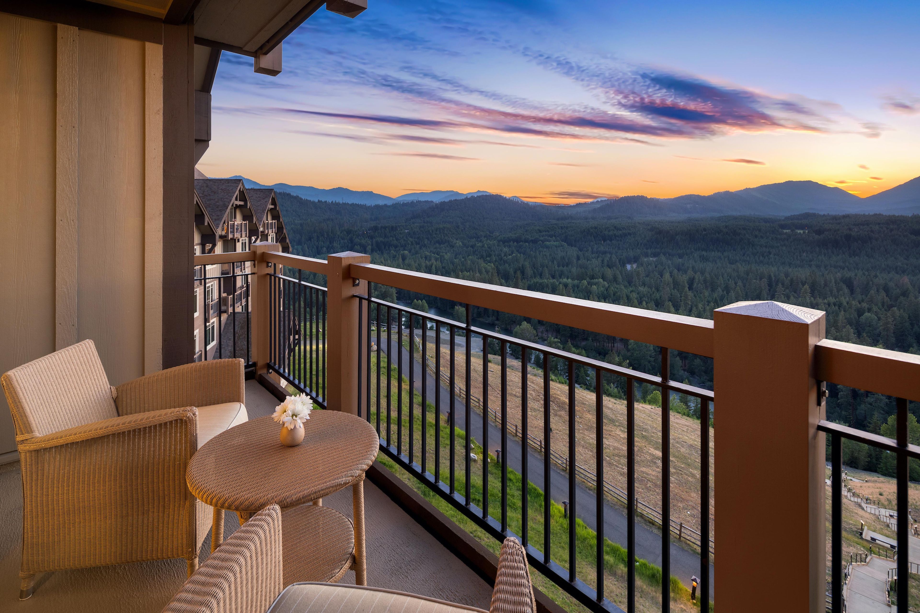 A balcony with wicker furniture and a view of a forested valley.