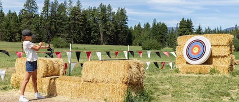 A person aiming an arrow at a hay bale with a target in the background.
