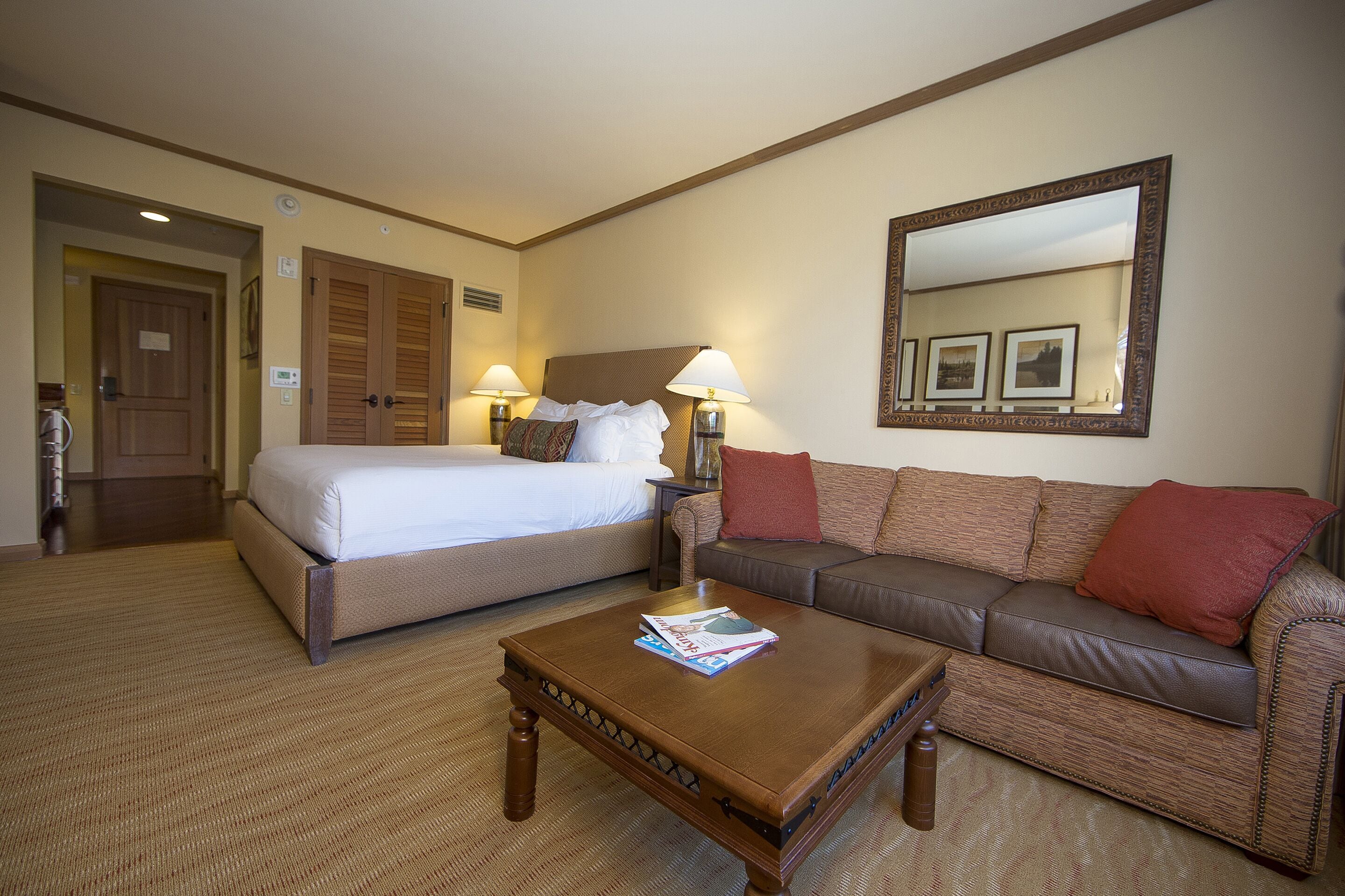 Ein Hotelzimmer mit einem Bett, einem braunen Ledersofa, einem Holztisch und einem großen Spiegel an der Wand.