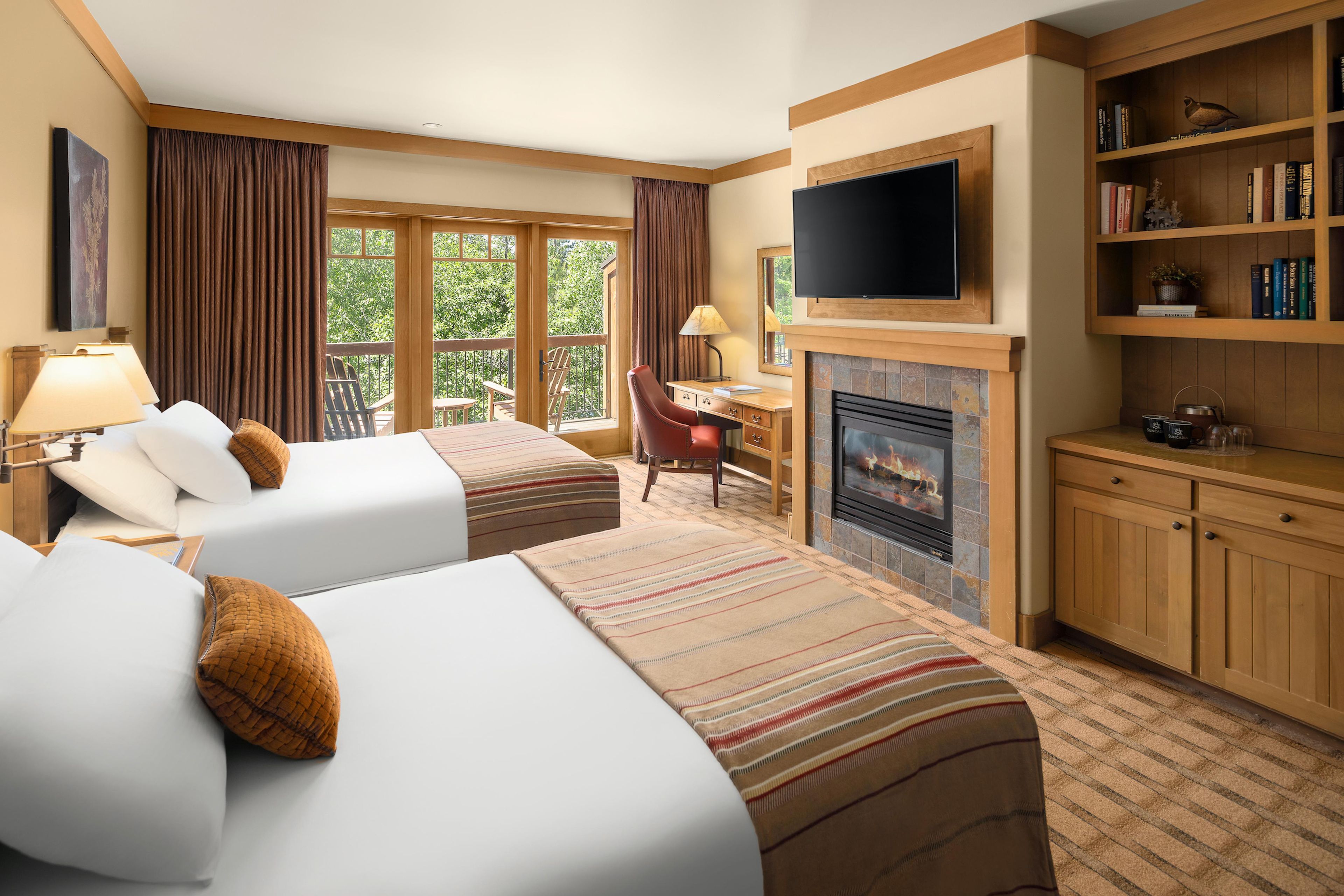 A hotel room with two beds, a television, a fireplace, and a bookshelf.