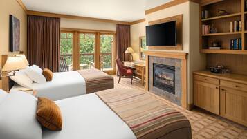 A hotel room with two beds, a television, a fireplace, and a bookshelf.