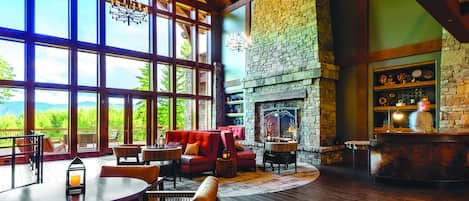 A spacious room with large windows, a stone fireplace, and a bar area.