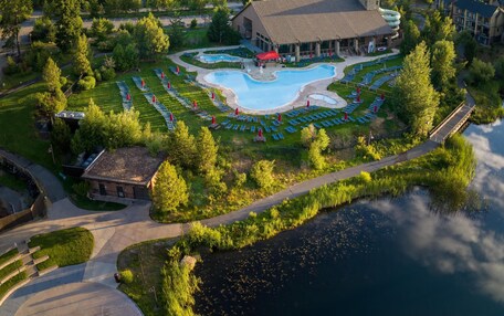 A resort with a swimming pool, a large building, and a forested area.