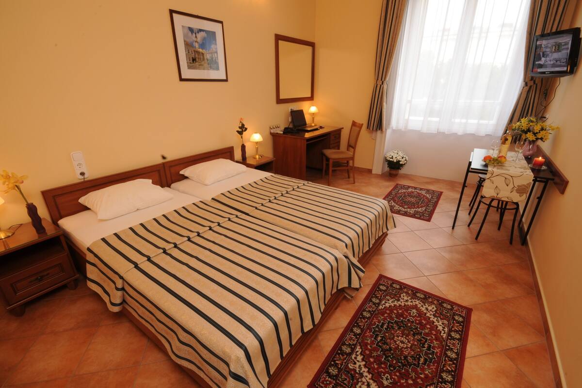 A hotel room with a large bed, a desk, a chair, a TV, and a window with curtains.
