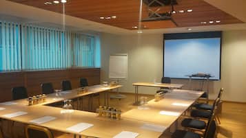 Ein Konferenzraum mit langen Tischen, Stühlen, einer Projektionsleinwand und einer Tafel.