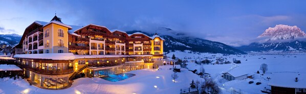 Un hotel grande de varios pisos con piscina, rodeado de montañas nevadas.