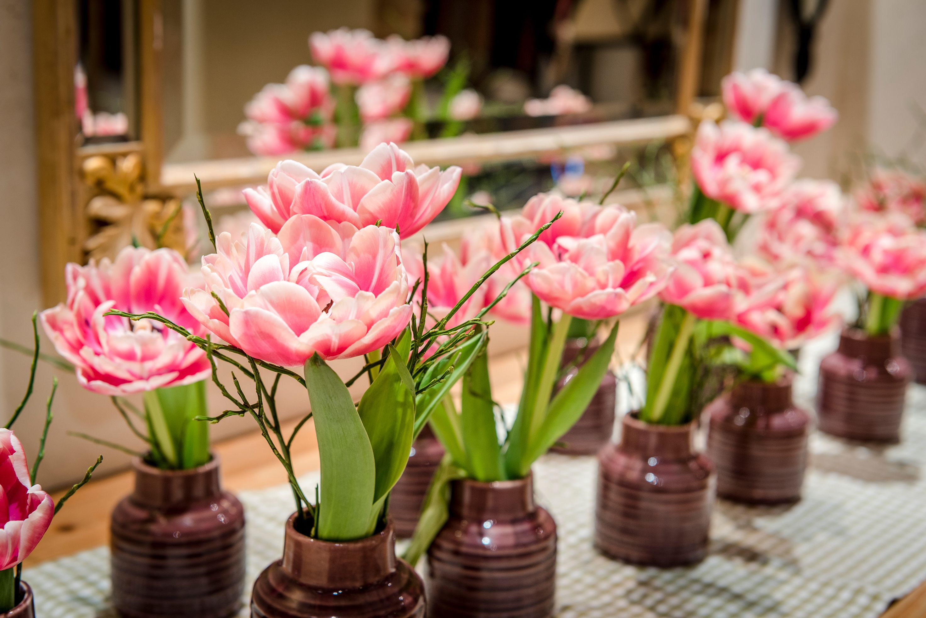 Flere små brune vaser med lyserøde blomster på et bord.