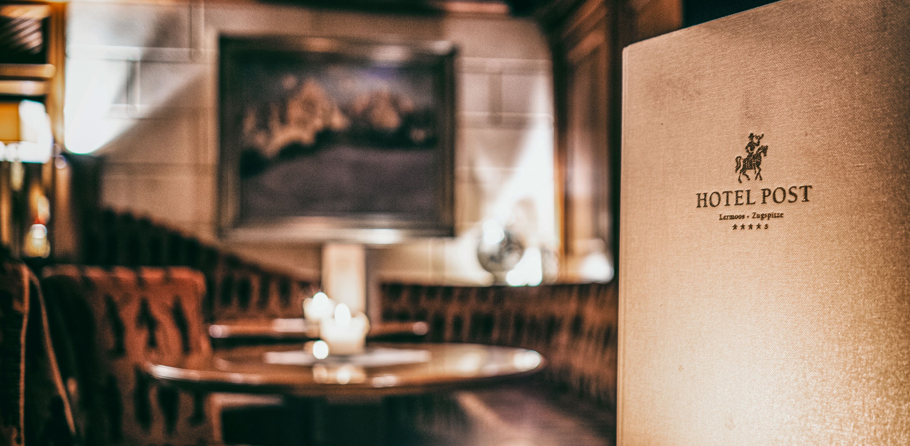 A blurred interior of a restaurant with a table and chairs, a candle, and a framed picture on the wall.