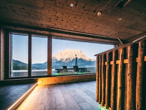 A room with large windows offering a mountain view, wooden flooring, and a wooden railing. - Hotel Post Lermoos (Lermoos)