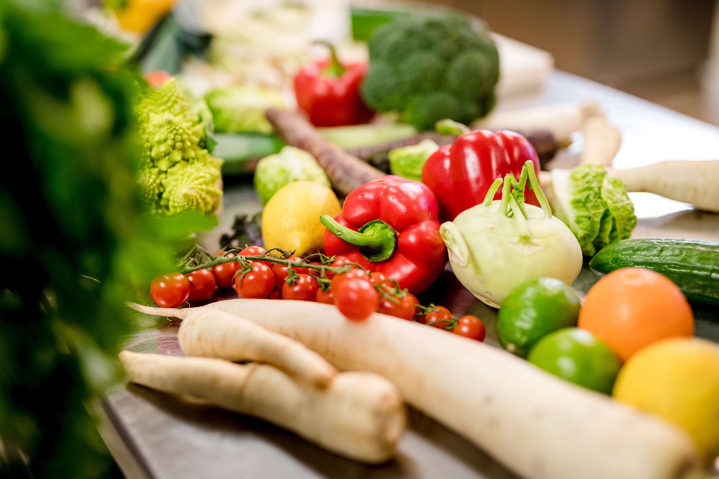 A variety of fresh vegetables including tomatoes, bell peppers, and artichokes on a wooden surface.
