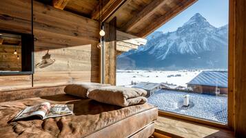 Ein gemütliches Zimmer in einer Holzhütte mit einem großen Fenster mit Blick auf einen verschneiten Berg.