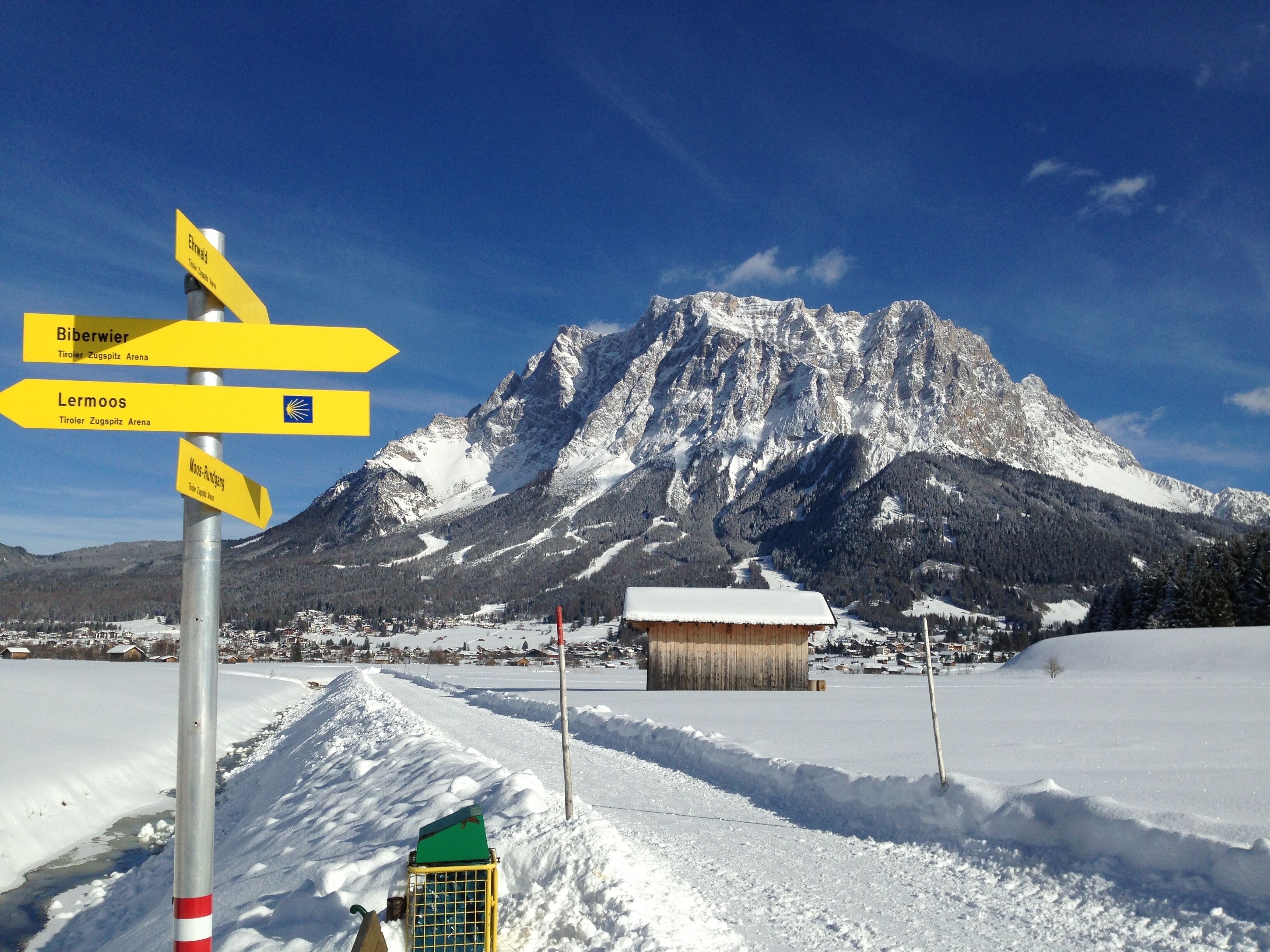 A snow-covered landscape with a mountain in the background and a signpost with directions to Biberwier, Lermoos, and Moos-Rundgass.