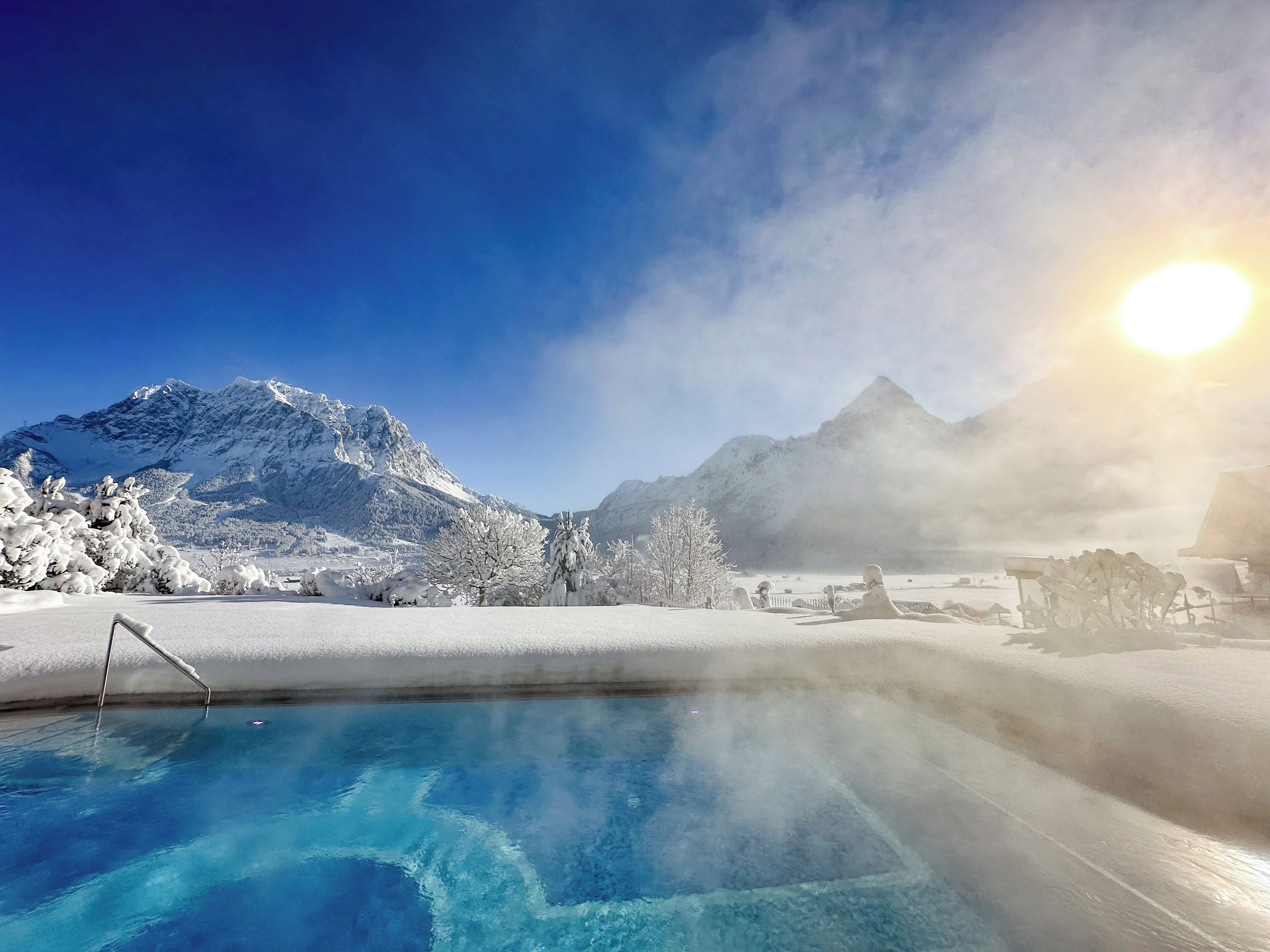 Una piscina azul cristalina rodeada de árboles nevados y montañas.