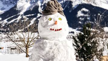 Ein Schneemann mit Schleife vor einer verschneiten Berglandschaft.