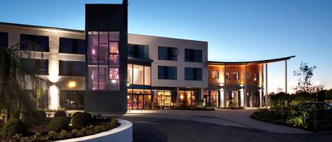 A modern hotel with a curved driveway, large windows, and a well-lit entrance.