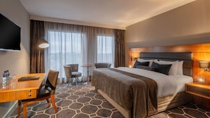 Habitación de hotel con cama, escritorio, silla, mesita y televisor.