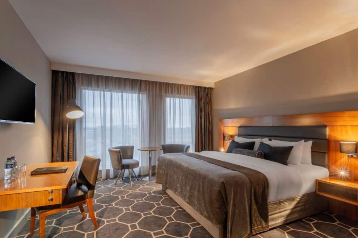 Ein Hotelzimmer mit Bett, Schreibtisch, Stuhl, kleinem Tisch und Fernseher.