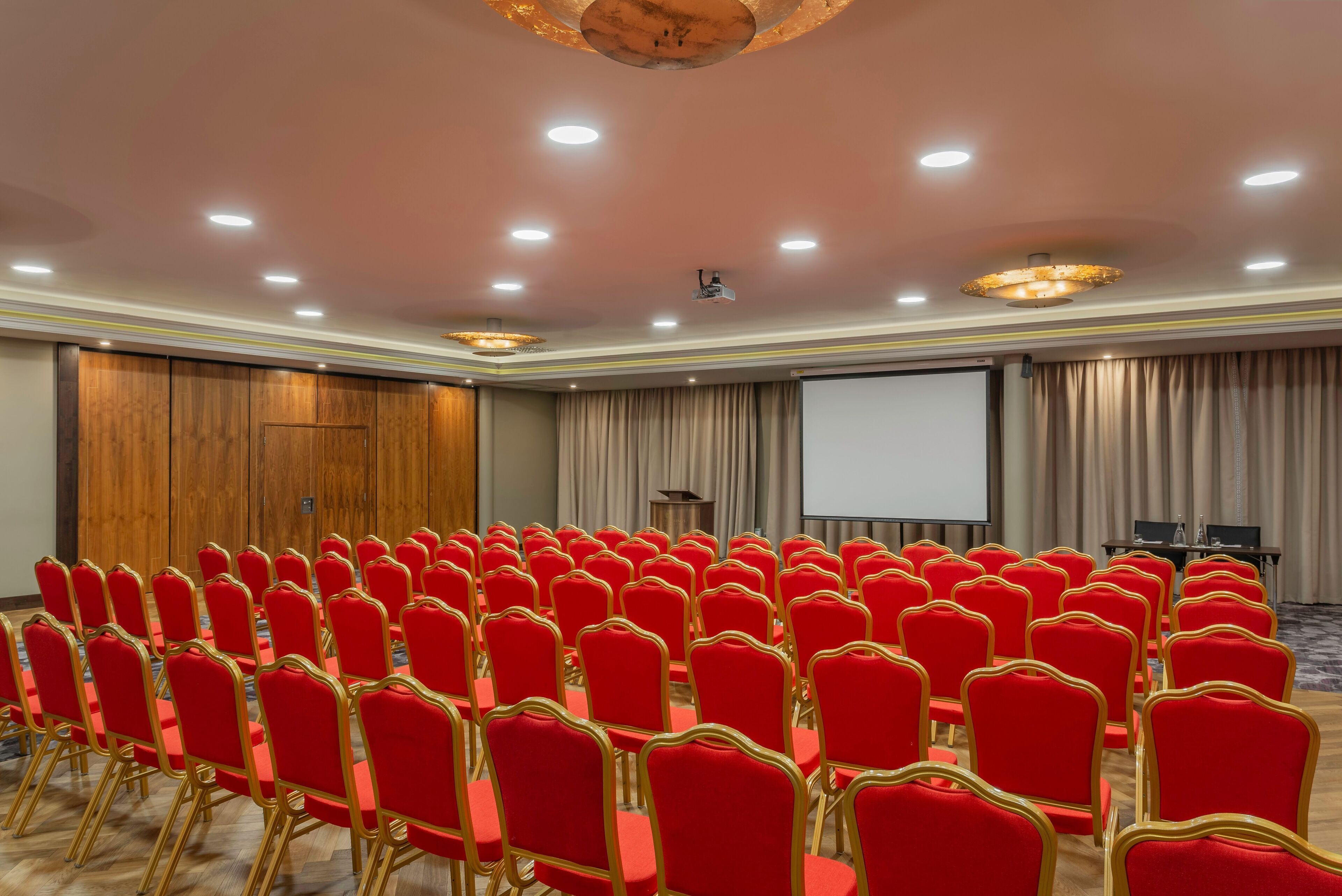 Uma sala de conferências com fileiras de cadeiras vermelhas e uma tela de projeção.