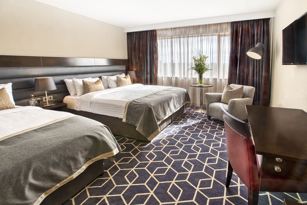 Ein Hotelzimmer mit zwei Betten, einem Schreibtisch, einem Stuhl, einem Fernseher und einem Fenster mit Vorhängen.