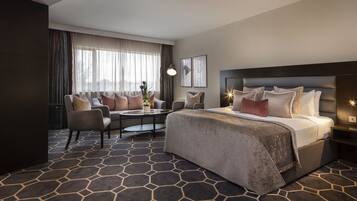 A hotel room with a large bed, a sofa, a coffee table, and a view of the outdoors.