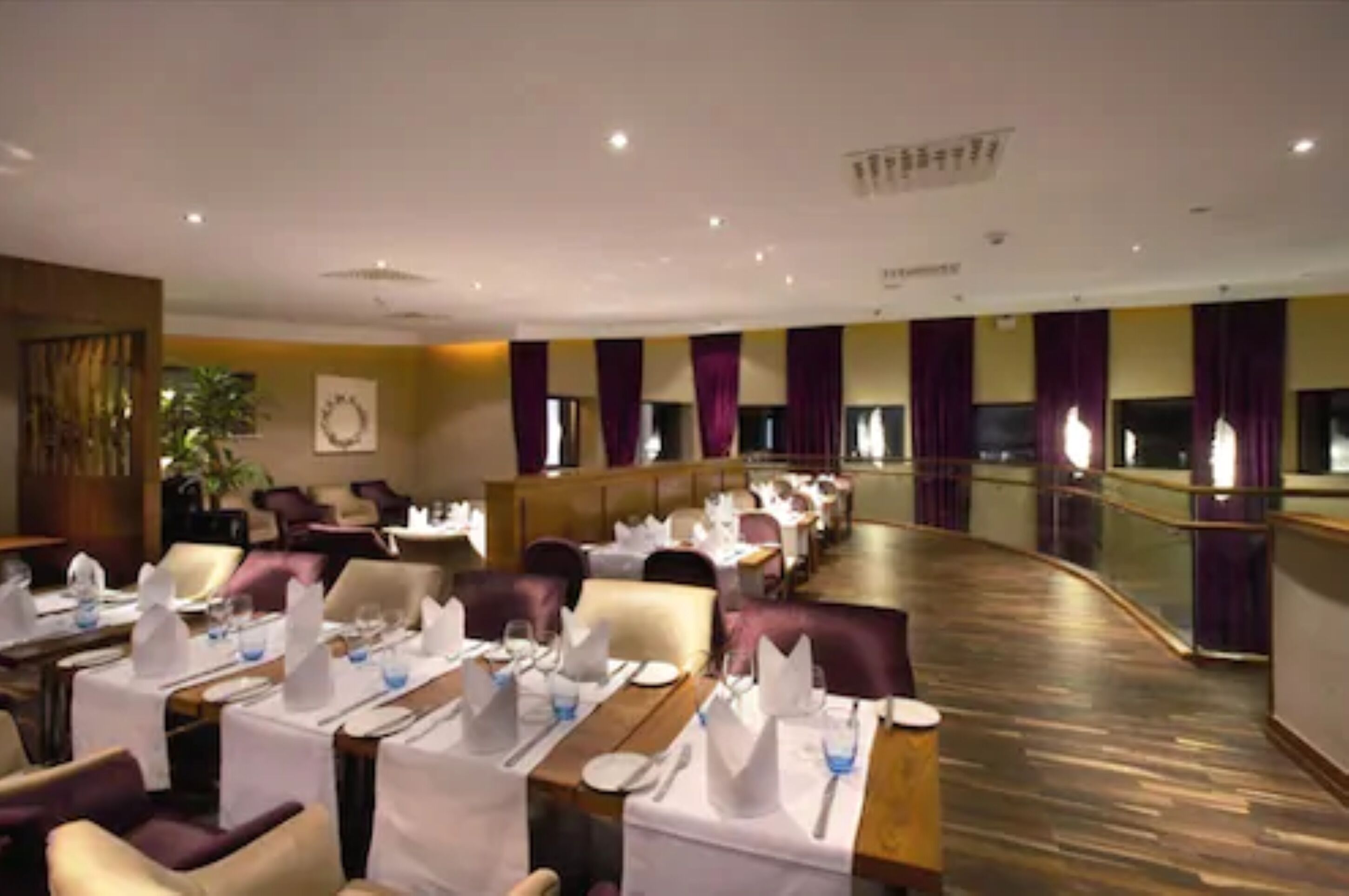 Un restaurante con mesas preparadas para comer, piso de madera curvada y cortinas moradas.