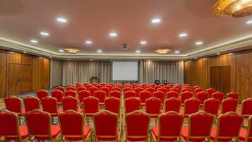 A conference room with rows of red chairs, a projector screen, and wooden paneling on the walls.