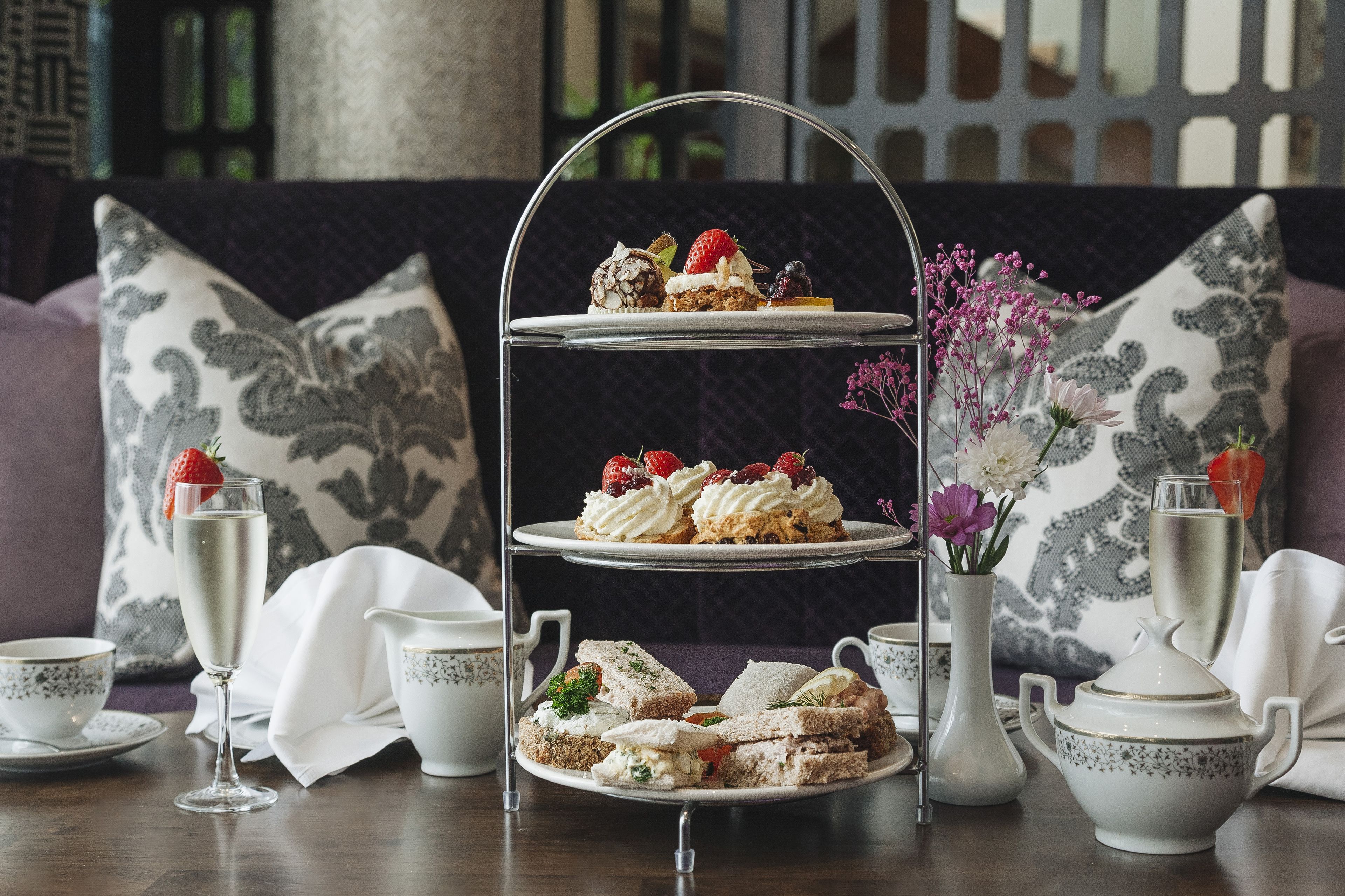 A tiered dessert stand with various pastries and sandwiches, accompanied by tea cups and a vase of flowers.