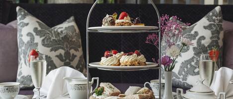 A tiered dessert stand with various pastries and sandwiches, accompanied by tea cups and a vase of flowers.