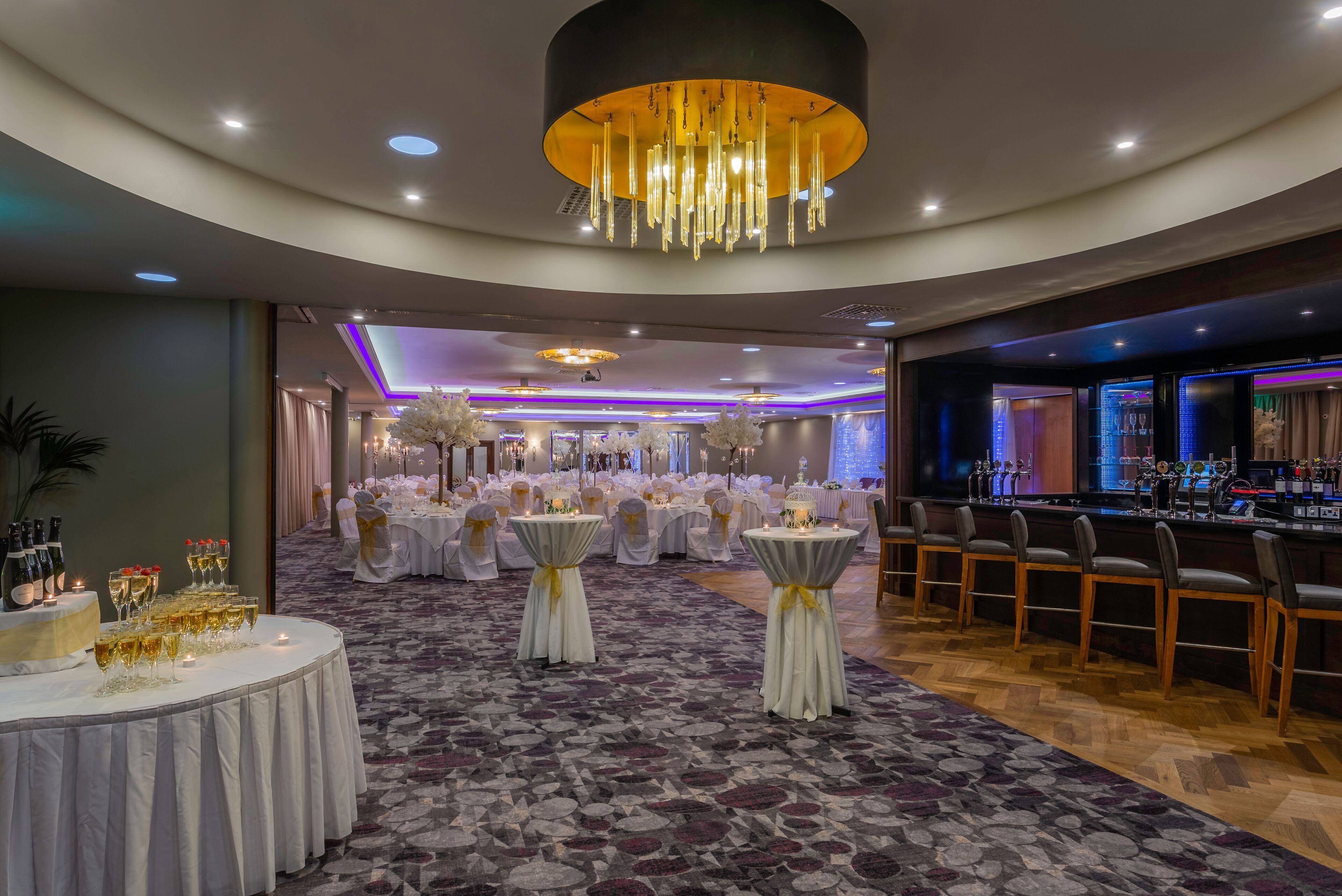 Een feestzaal met ronde tafels, een bar en een kroonluchter.