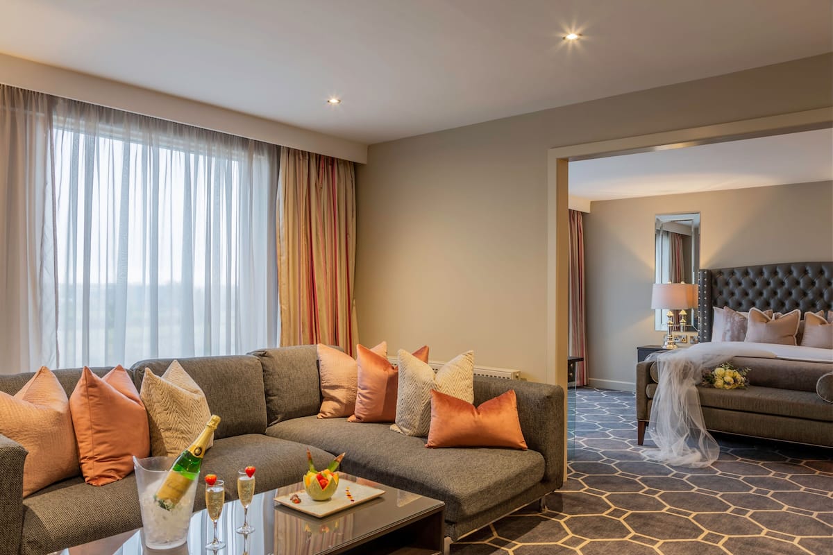 Ein Hotelzimmer mit grauem Sofa, einem Couchtisch mit Champagner und einem Himmelbett.
