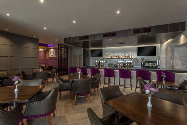 A modern bar area with a long counter, multiple seating options, and a television screen. - Athlone Springs Hotel (Athlone)