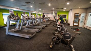 Ett gym med flera löpband och motionscyklar, en grön vägg och en klocka på väggen.