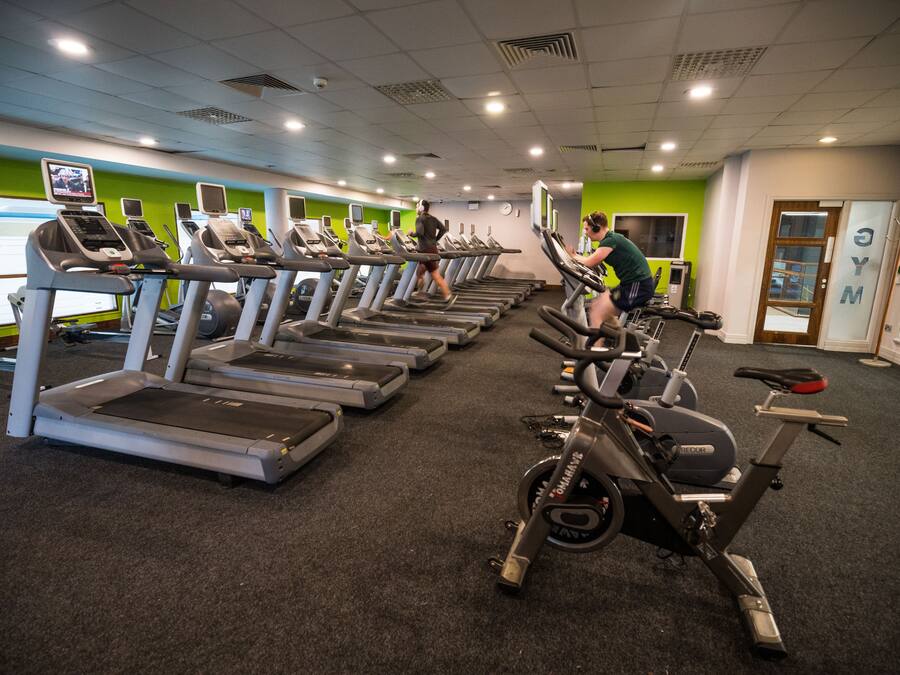 Ett gym med flera löpband och motionscyklar, en grön vägg och en klocka på väggen.