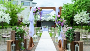 Un pasillo nupcial al aire libre con un arco de madera decorado con flores y cortinas blancas.