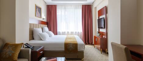 A hotel room with a bed, a desk, a chair, a TV, and a window with curtains.