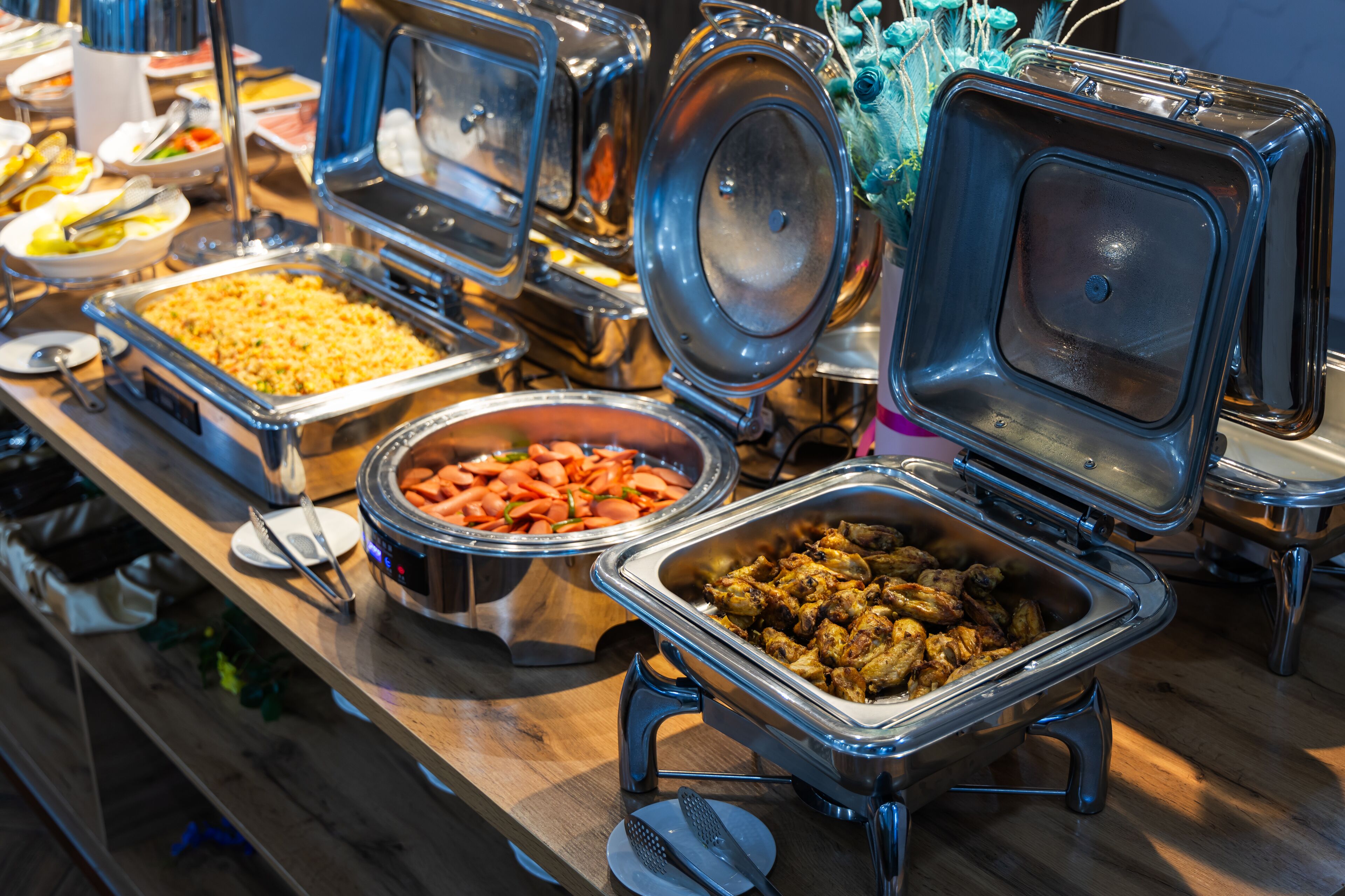 A buffet with various dishes including a large container of rice, a bowl of carrots, and a tray of meat.
