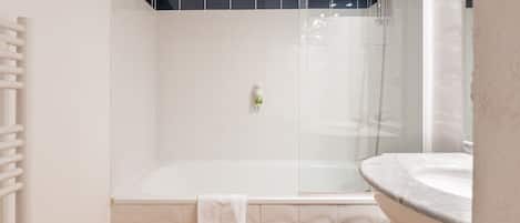 Un baño moderno con ducha envuelta en vidrio, un lavabo blanco y un perchero para toallas.