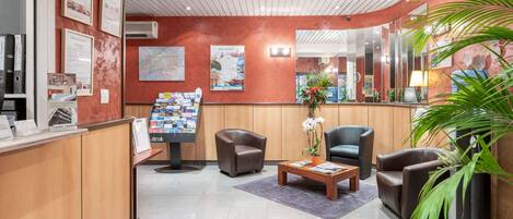 A reception area with a wooden counter, two leather armchairs, a coffee table, and a large mirror.